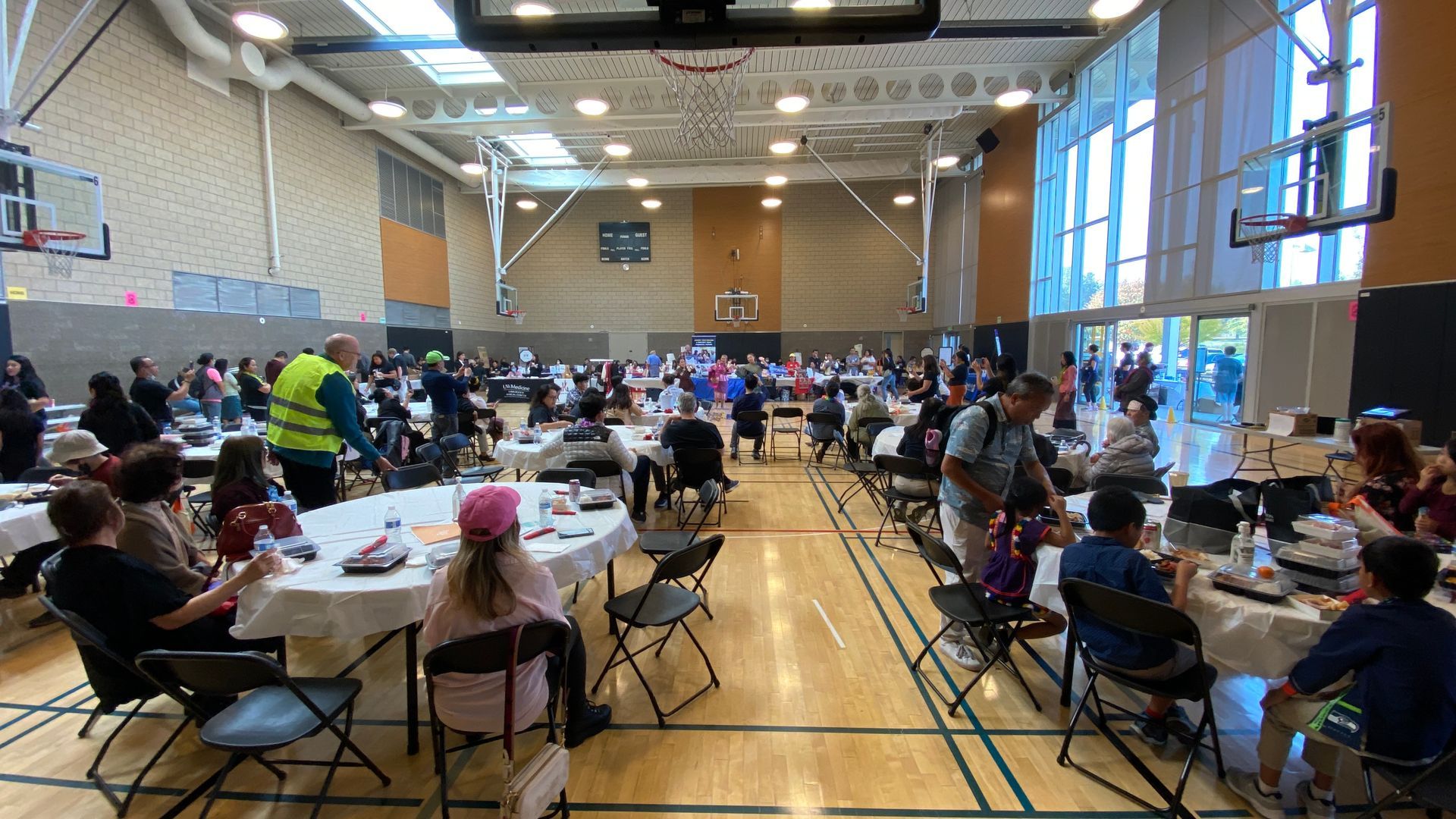 A large group of people are sitting at tables in a gym.