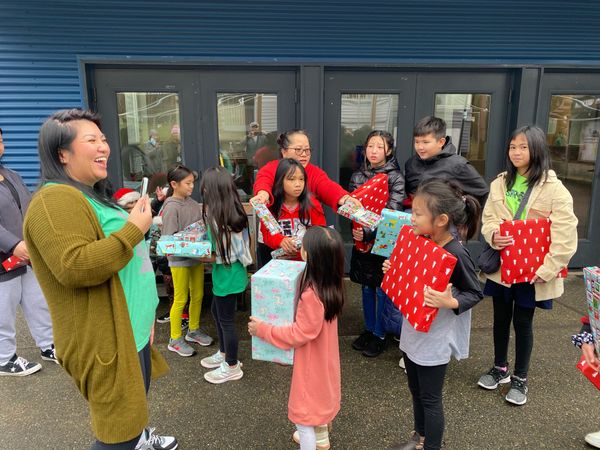 A group of children are standing in front of a building holding presents.