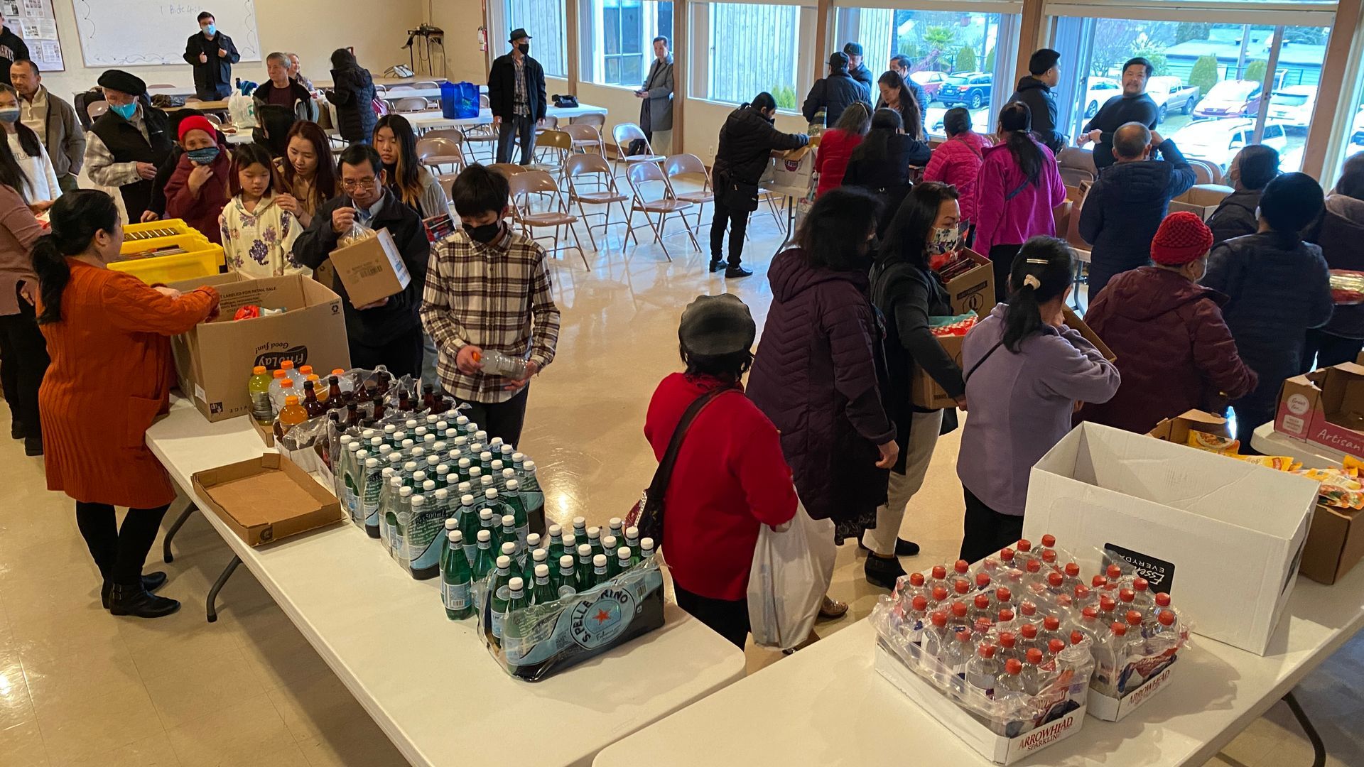 A large group of people are standing around tables filled with food and drinks.