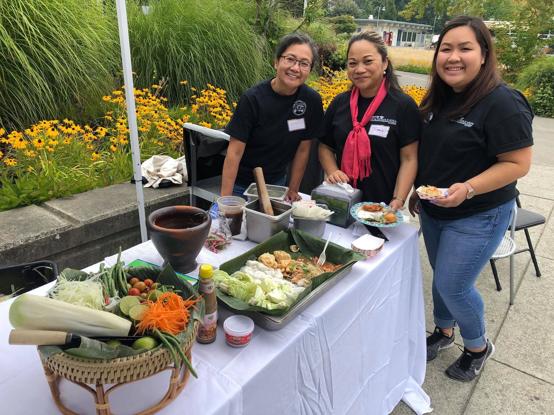 Three women are standing around a table filled with food.