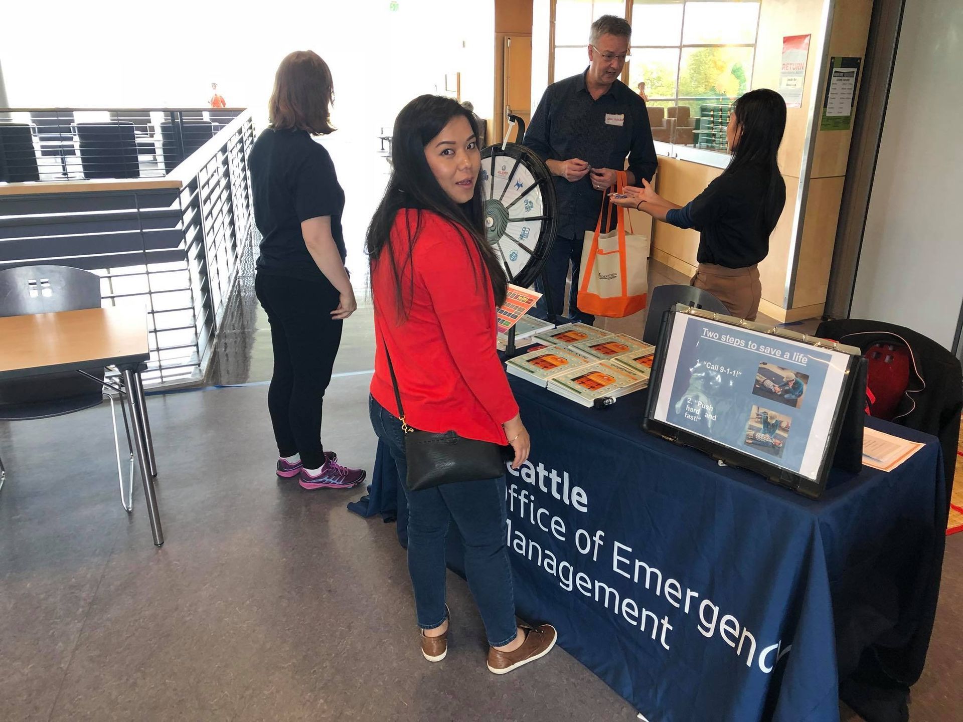 A woman in a red shirt is standing in front of a table that says emergency management.