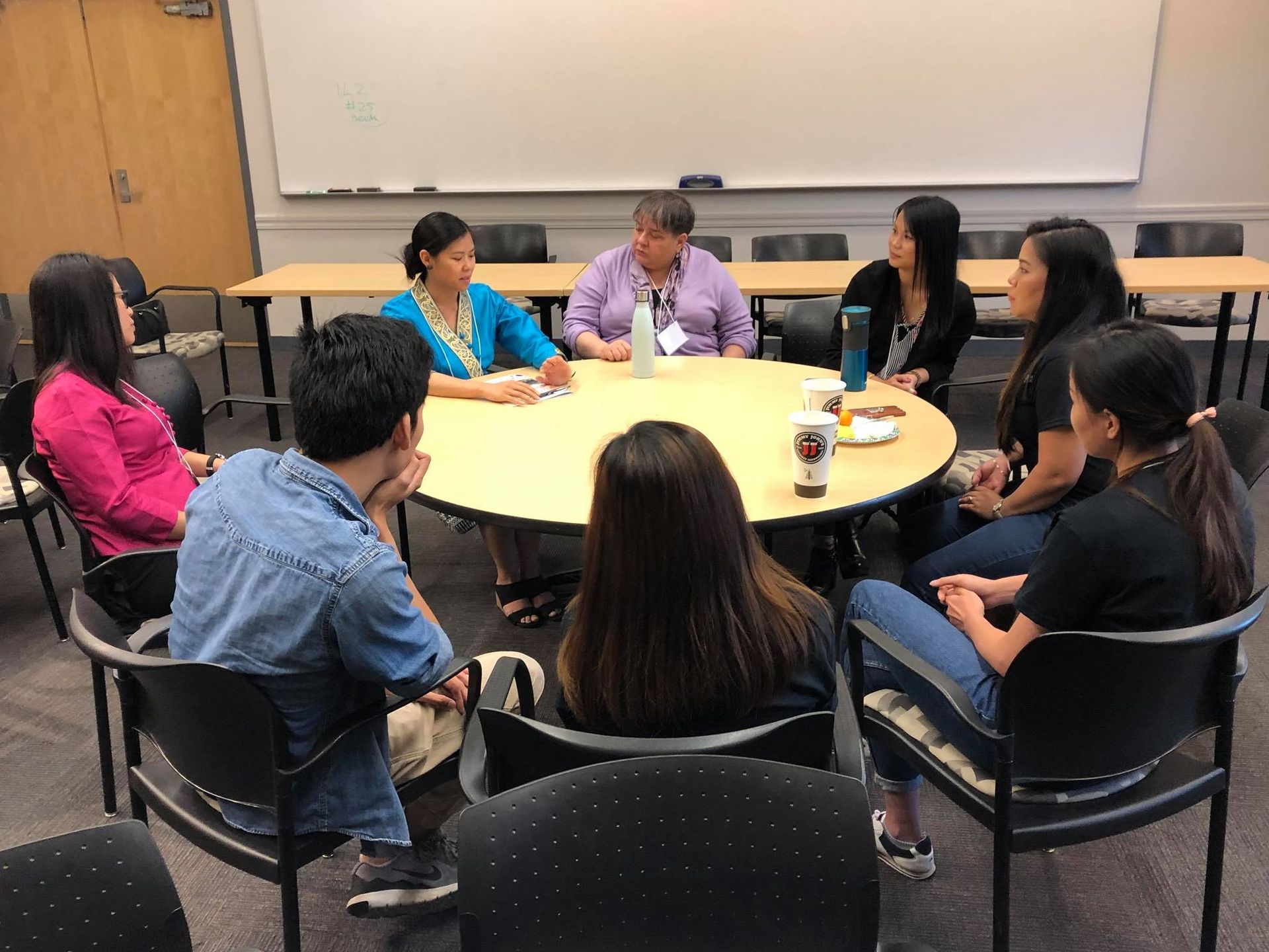 A group of people are sitting around a table in a classroom.