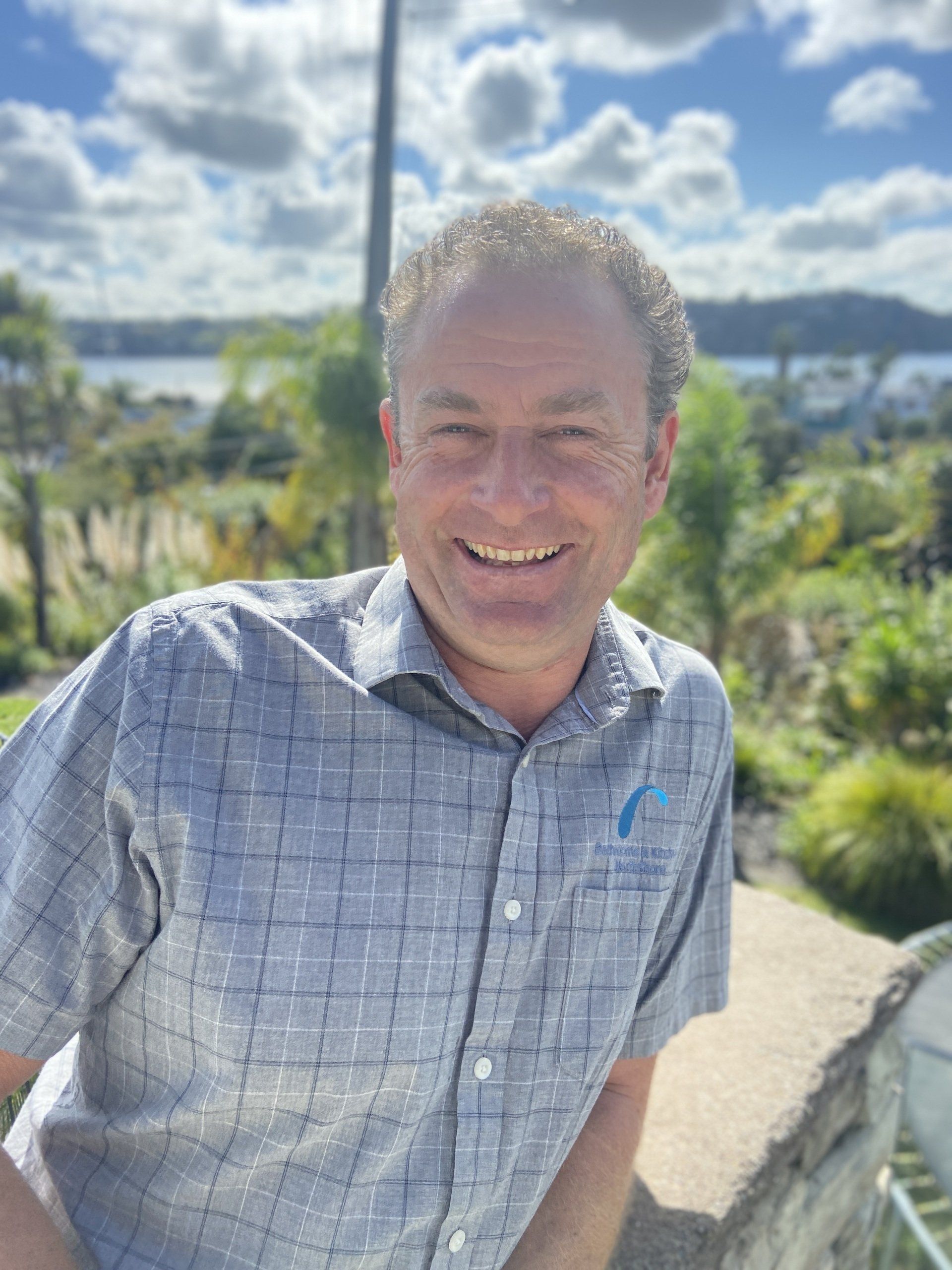 A man in a plaid shirt is smiling for the camera while standing next to a wall.