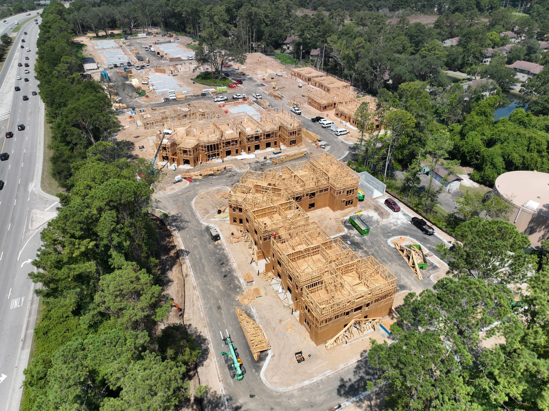 Aerial view of a construction site with wooden framing, dirt roads, and trees surrounding the area.
