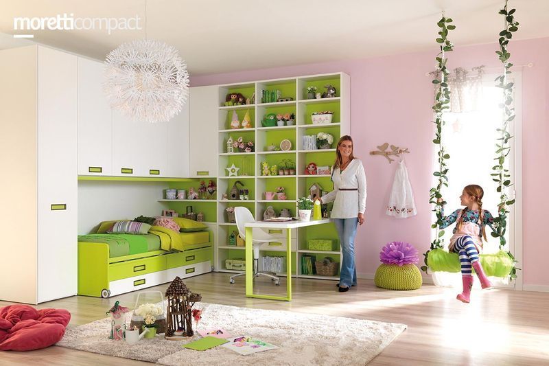 Sala giochi con mobili verde lime, una donna vicino a degli scaffali e un bambino che corre vicino a una finestra luminosa.