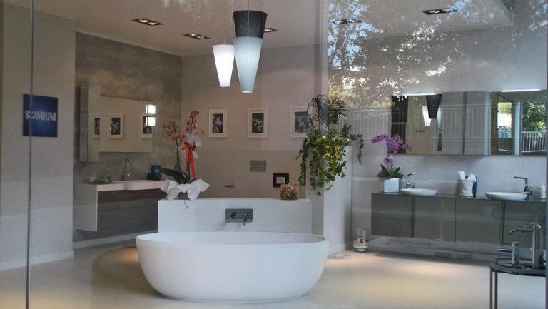 Showroom di bagni moderni con vasca bianca freestanding, doccia in vetro e mobile lavabo con fiori.