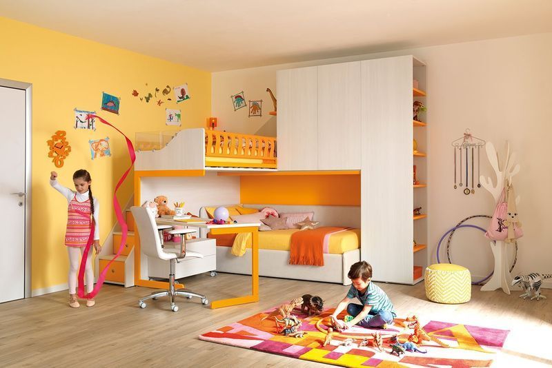 Bambini che giocano in una camera da letto colorata con letti a castello, una scrivania e giocattoli sul pavimento.