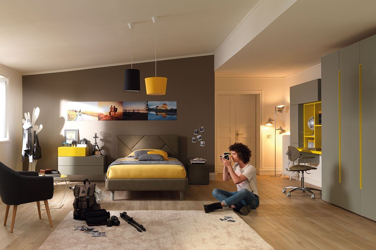 Camera da letto moderna con letto giallo, parete d'accento scura e una persona seduta sul pavimento.