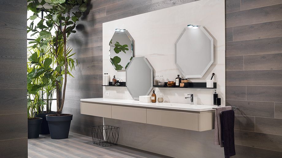 Mobile bagno moderno con doppio specchio ottagonale, piano lavabo bianco e piante da interno vicino alla finestra.