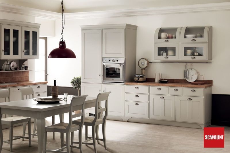 Cucina-sala da pranzo luminosa e bianca con tavolo in legno, lampada a sospensione, armadietti e forno a incasso.