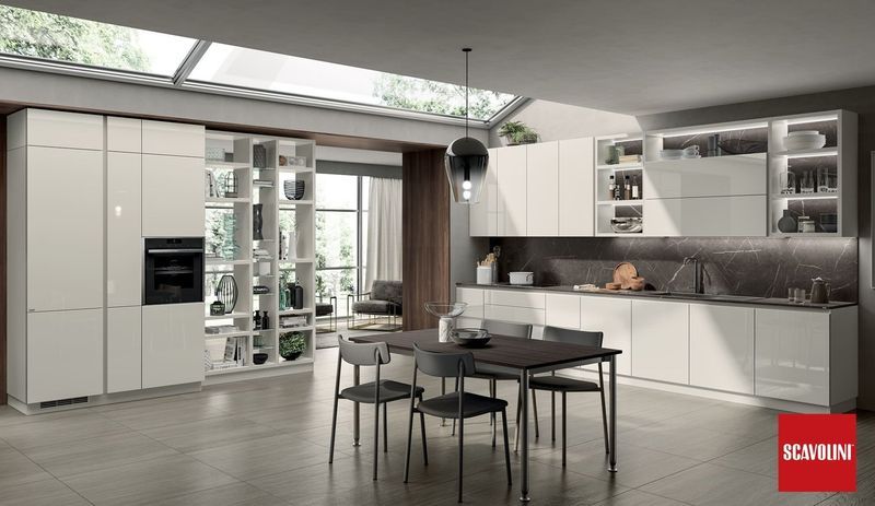 Cucina moderna bianca con isola, tavolo da pranzo e pensili con ante in vetro.