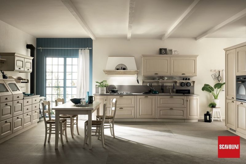 Cucina color crema luminoso con tavolo da pranzo, tende blu alle finestre e luce del sole che filtra sul pavimento