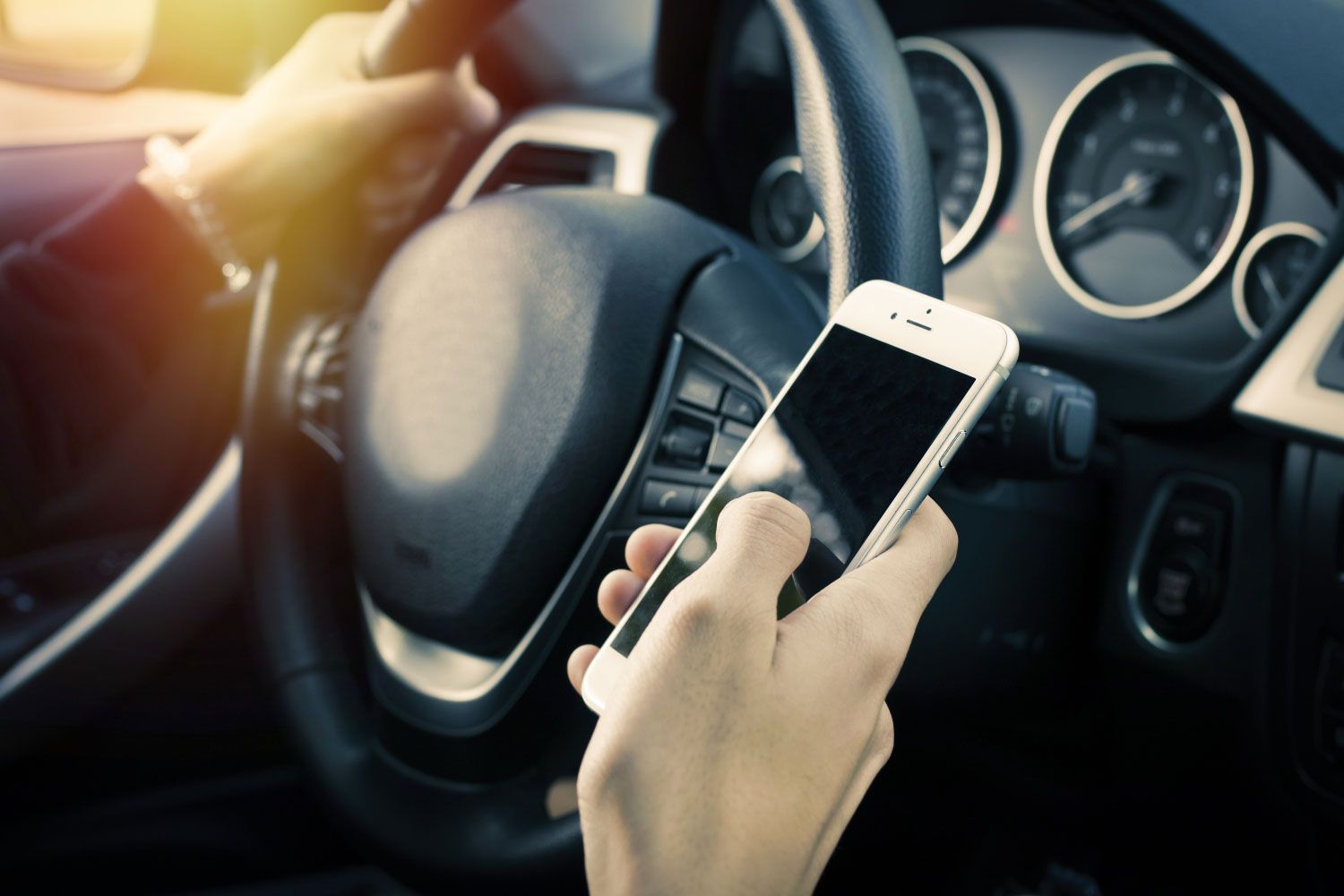 Driver holding a smartphone while behind the wheel, illustrating distracted driving