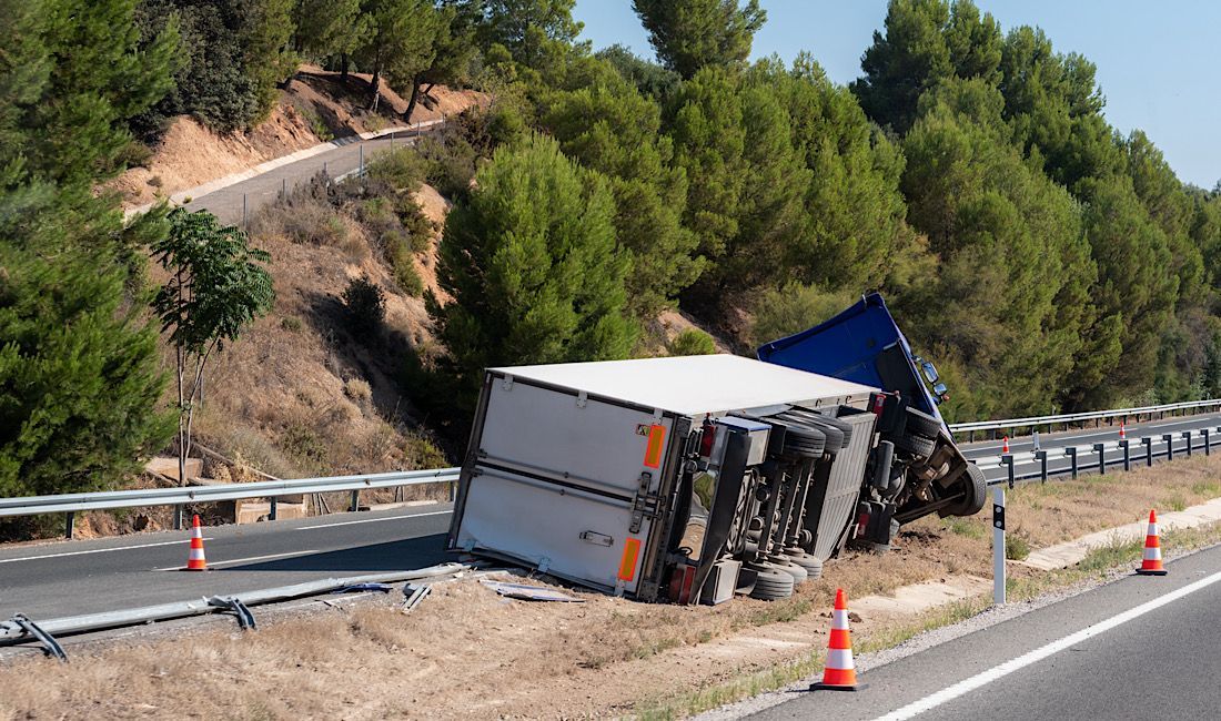 Truck accident on the highway. Truck laying on its side after a sharp turn around the bend. Caution cones along the truck.