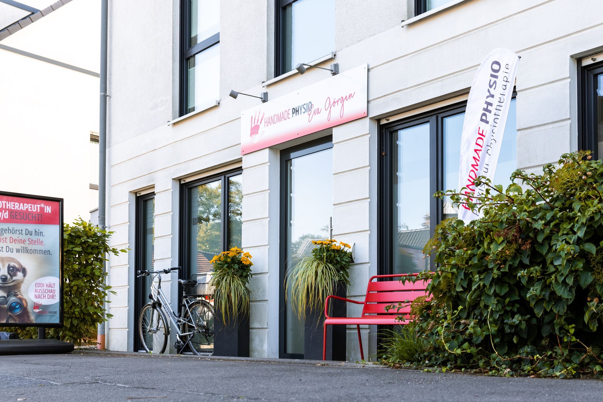 Außenansicht der Physiopraxis mit Blumenkübeln und roter Sitzbank