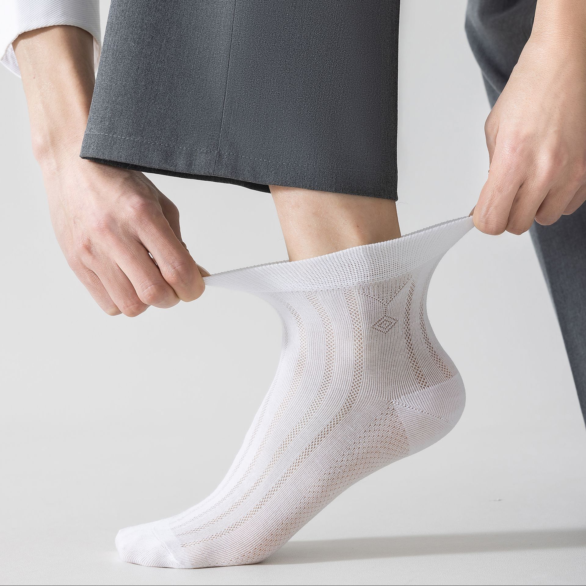 Person pulling up a white lacy sock over their foot, gray pants visible.