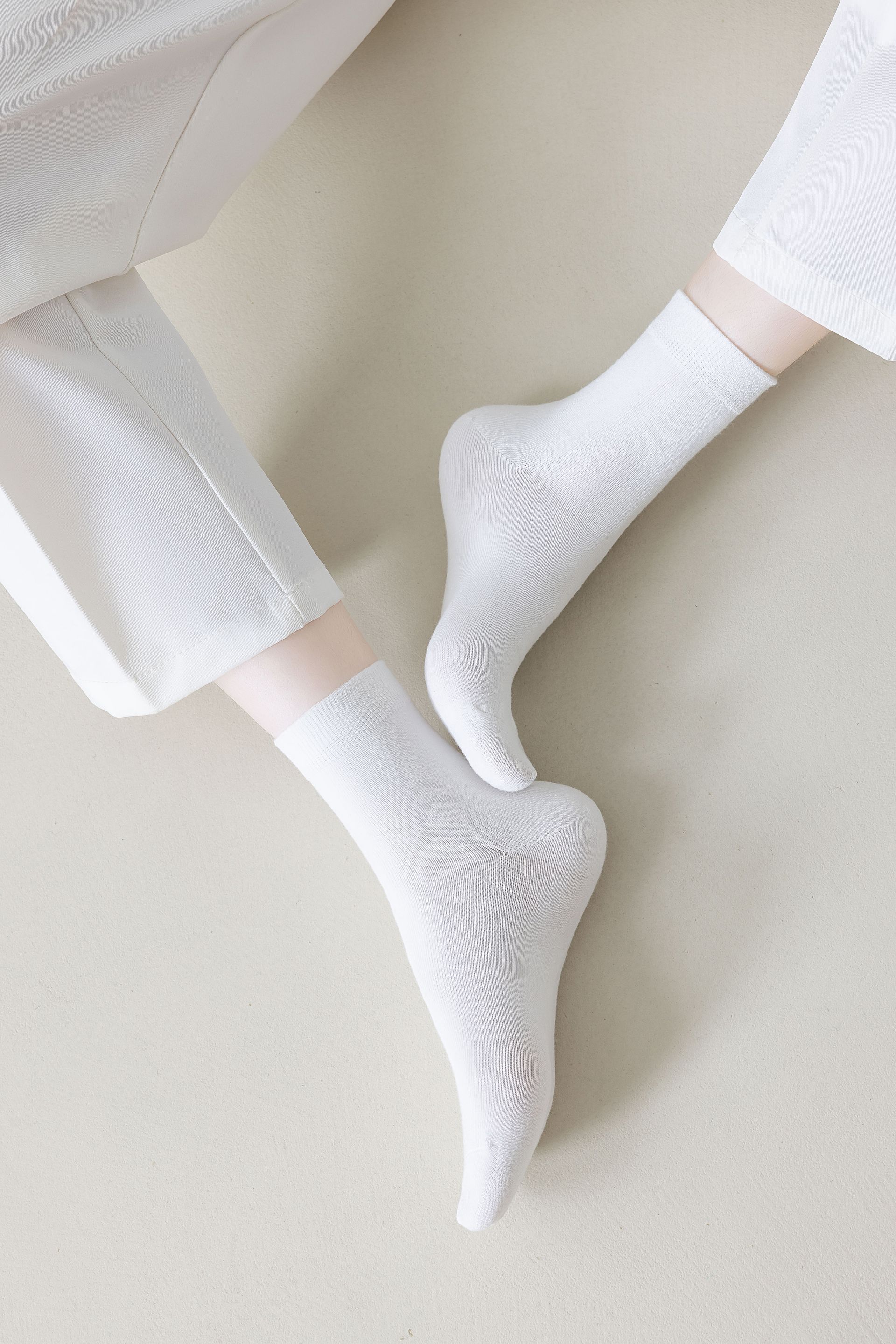 Pair of feet in white patterned socks, white pants, neutral background.