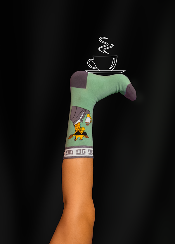 A person's leg with a green sock featuring a pouring coffee design balanced with a coffee cup illustration on a black background.