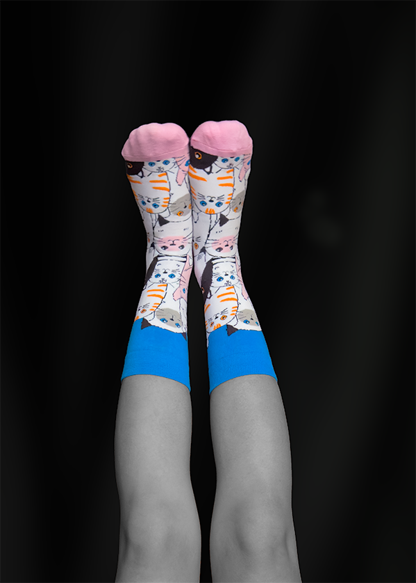 Legs with cat-patterned socks, blue cuffs, against a black background, legs crossed.