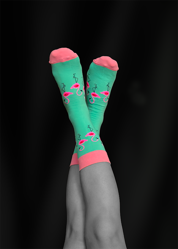 Legs crossed, wearing teal socks with flamingoes, and pink toes.