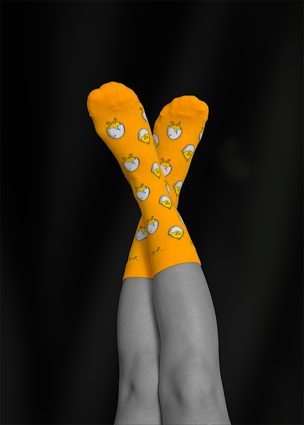 Crossed legs wearing bright orange socks patterned with white chickens against a black background.