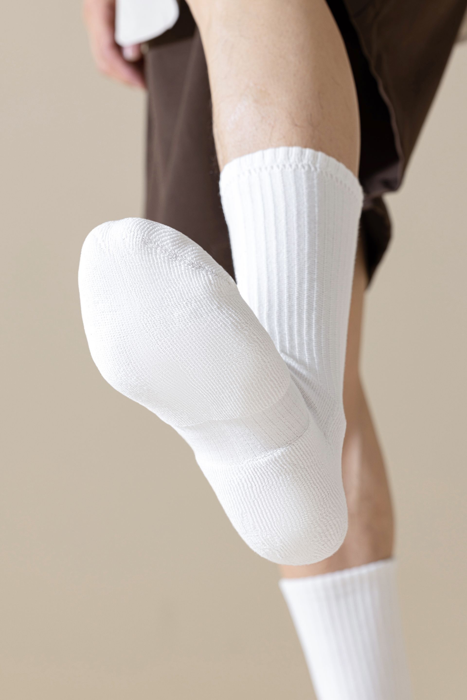 Pair of white socks on legs, against a tan background.