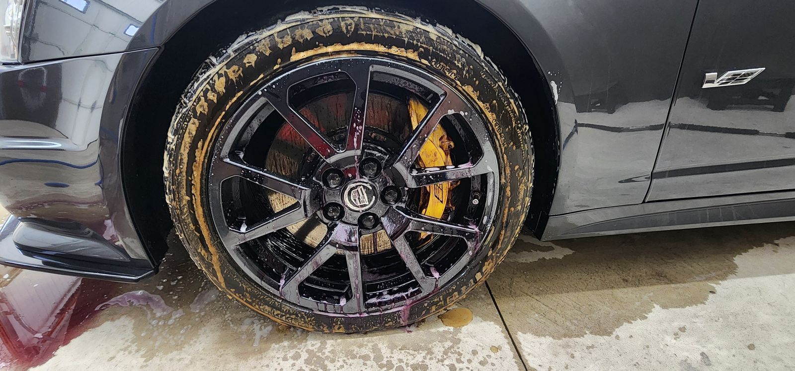 Black car tire with black rims, yellow brake calipers, and mud.