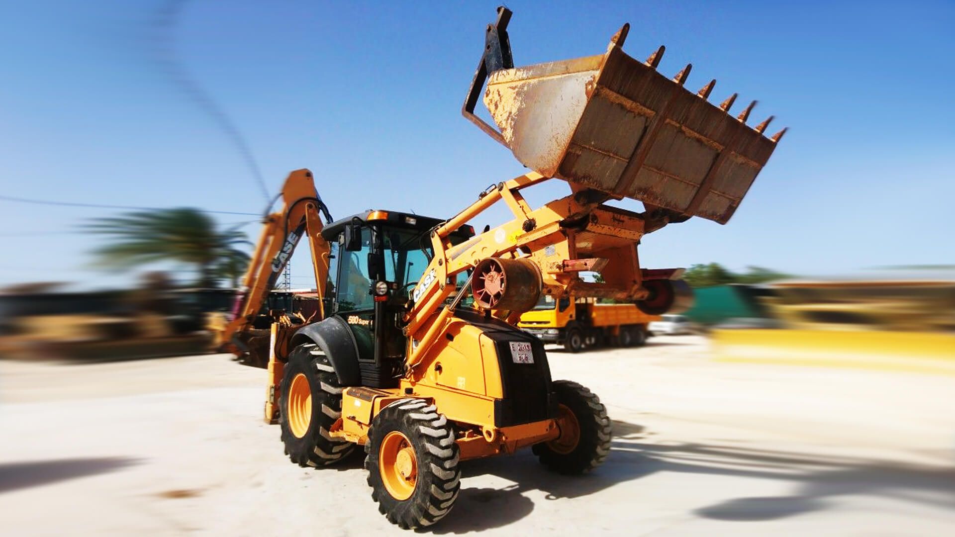 A yellow tractor with a large bucket is driving down a road