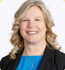 Woman with long blonde hair smiles, wearing a patterned top and black blazer, in front of a colorful backdrop.