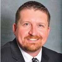 Man with auburn hair and beard in a suit, smiling, looking at the viewer.