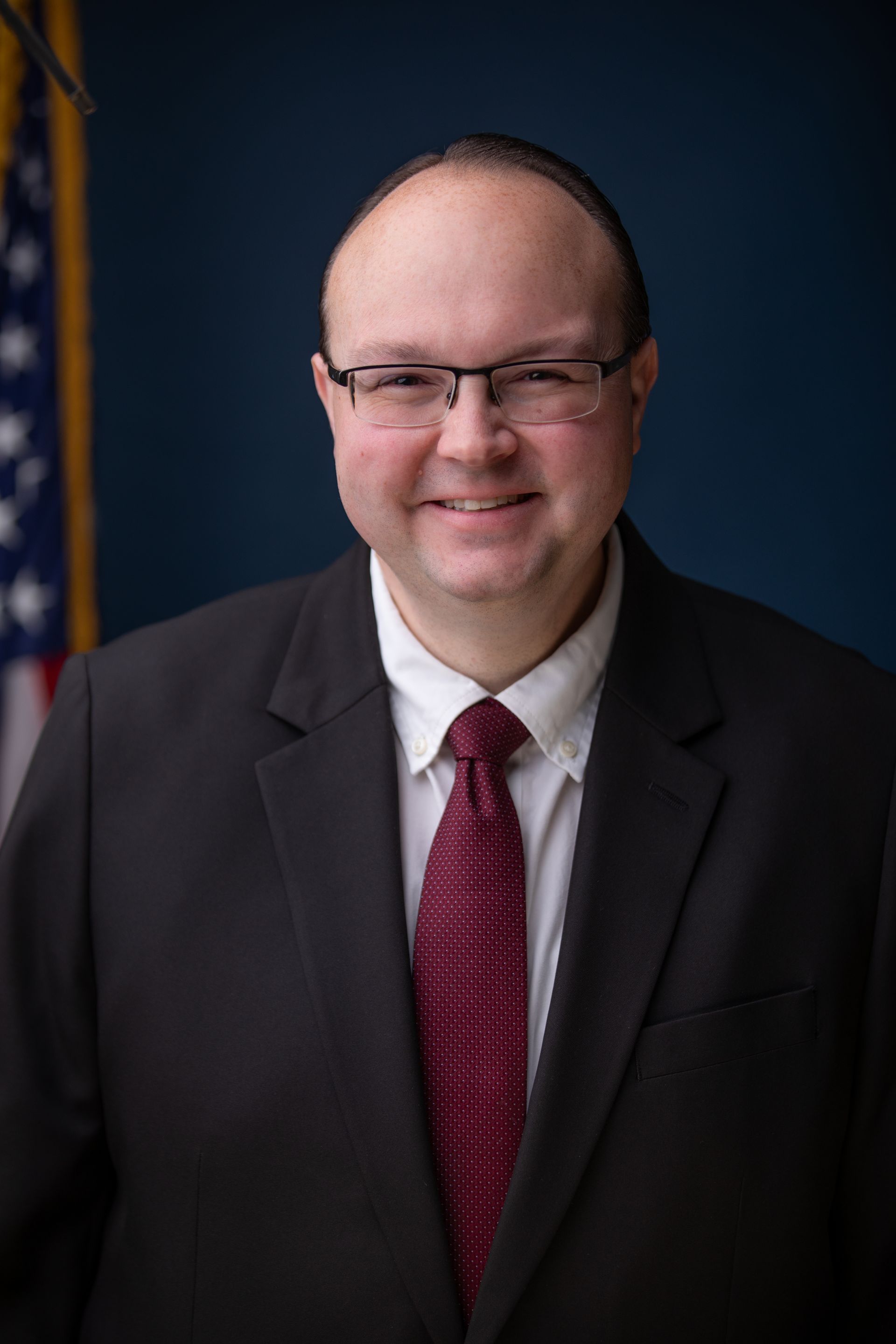 Man in a blue suit smiling, wearing a patterned blue tie.