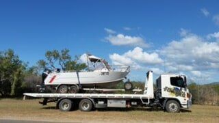 A Tow Truck Is Carrying A Boat On The Back Of It — Day & Night Towing & Transport In Ingham, QLD