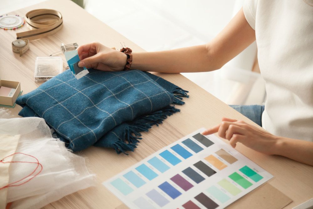 A Woman Is Sitting At A Table Looking At A Swatch Of Fabric  — Gympie Embroidery Services In Southside, QLD