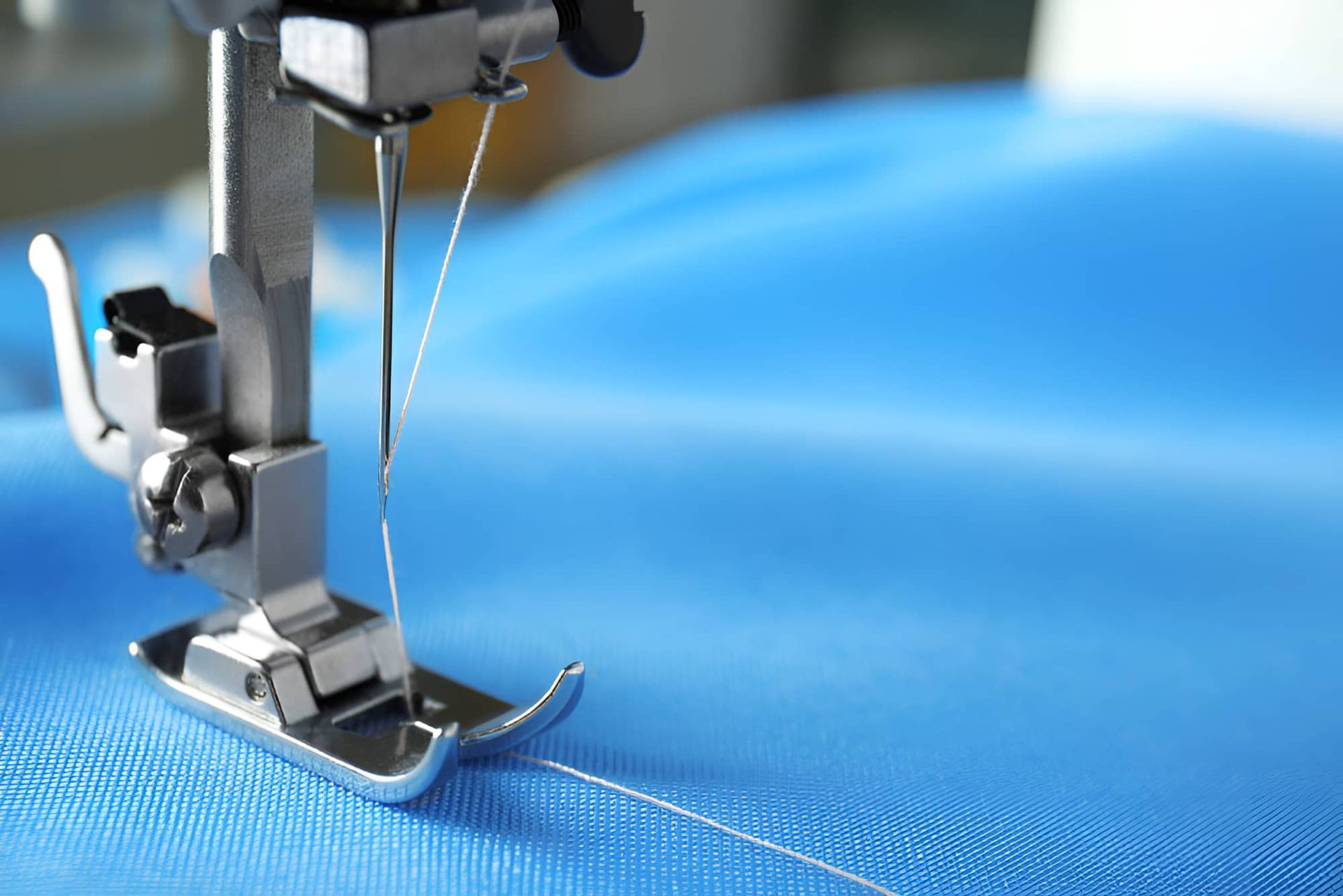 A Sewing Machine Is Stitching A Piece Of Blue Fabric — Gympie Embroidery Services In Southside, QLD