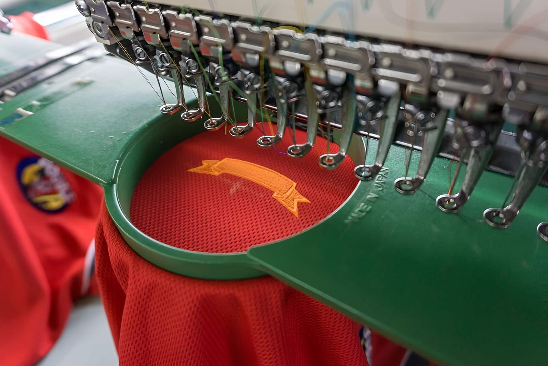 A Close Up Of A Machine That Is Embroidery A Logo On A Red Shirt — Gympie Embroidery Services In Southside, QLD