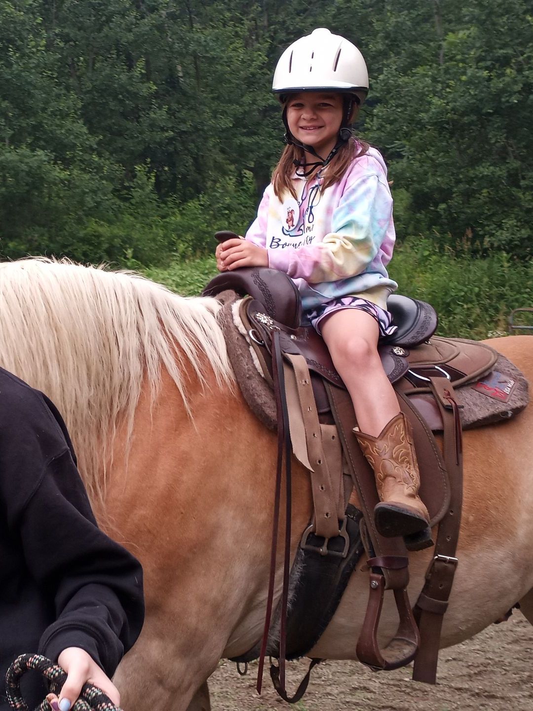 A little girl wearing a helmet is riding a horse
