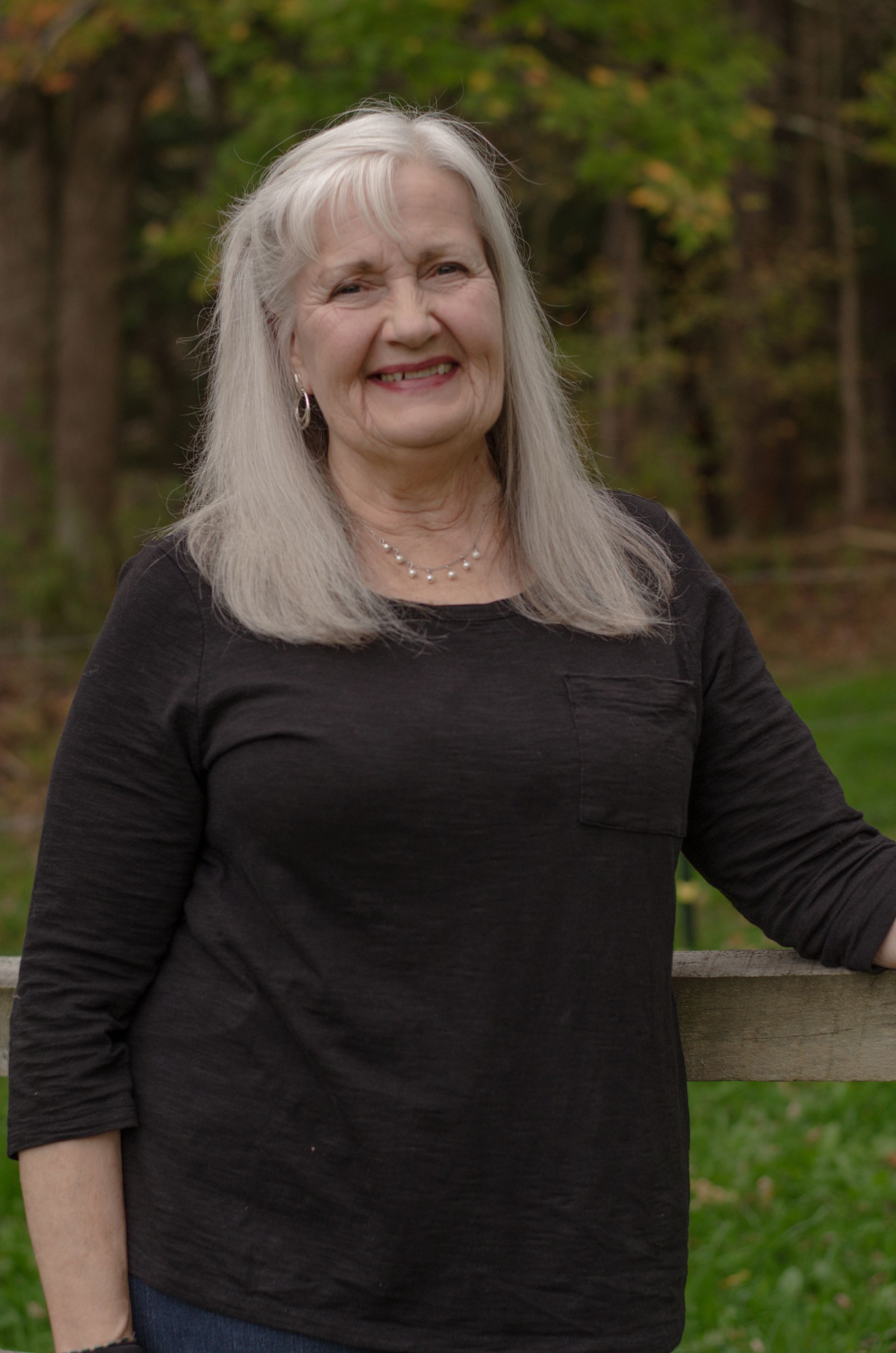 A woman wearing a green shirt and a black jacket is standing in a park.