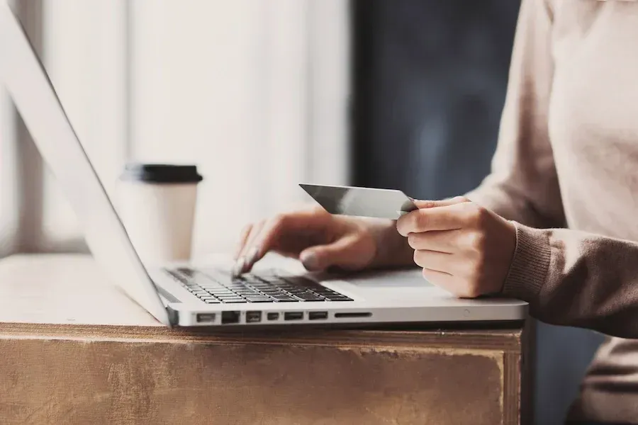 A woman is holding a credit card while using a laptop computer.