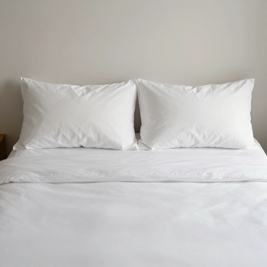 Neatly made bed with white sheets and two white pillows against a plain beige wall
