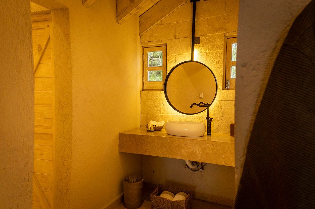 Bathroom with stone sink, round mirror, and warm lighting.