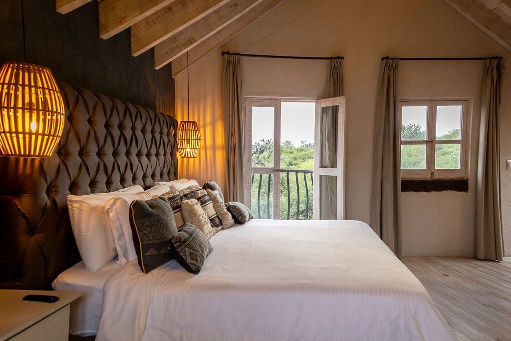 Bedroom with a large bed, tufted headboard, and open French doors overlooking greenery.