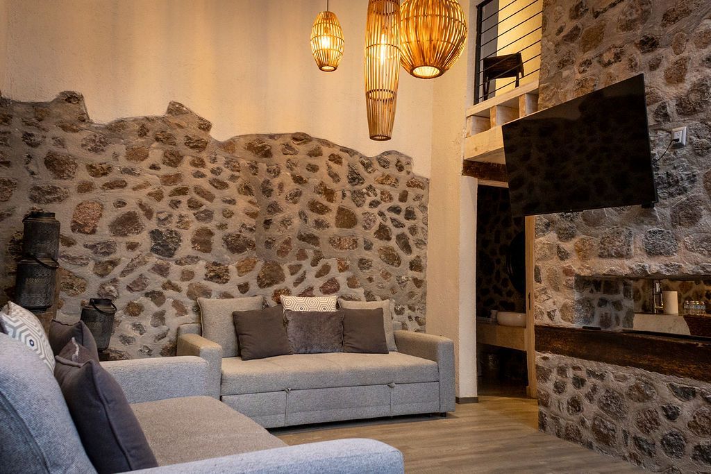Living room with stone walls, gray sofa, hanging lights, and a mounted TV.