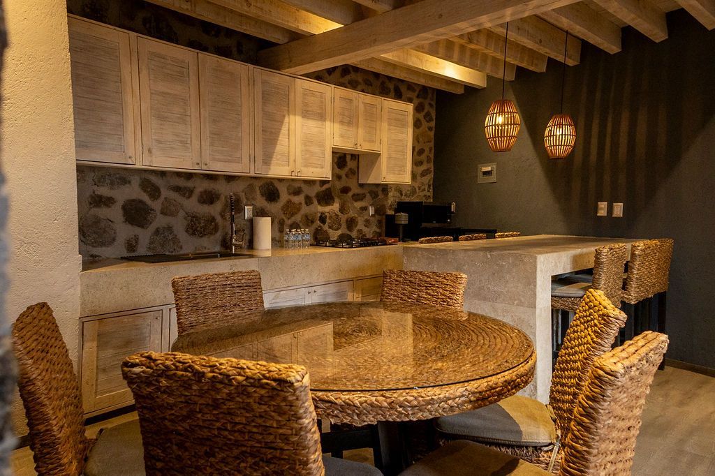 Outdoor kitchen with stone walls, wooden cabinets, and a round dining table with woven chairs.