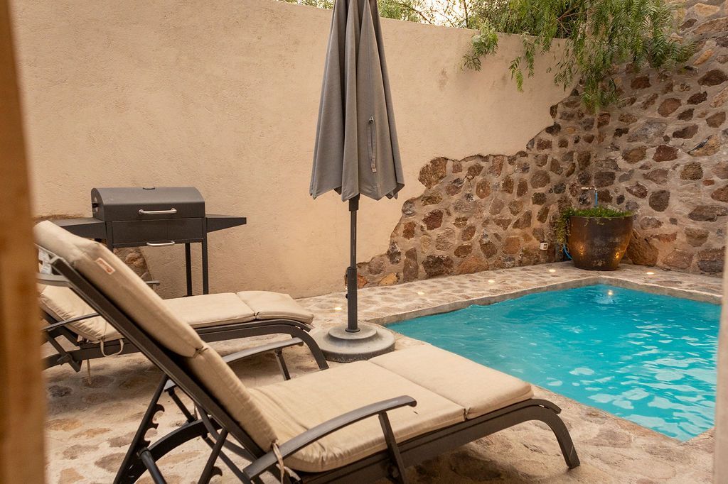 Lounge chairs near a small pool and a grill in a stone-walled patio. Umbrella is closed.