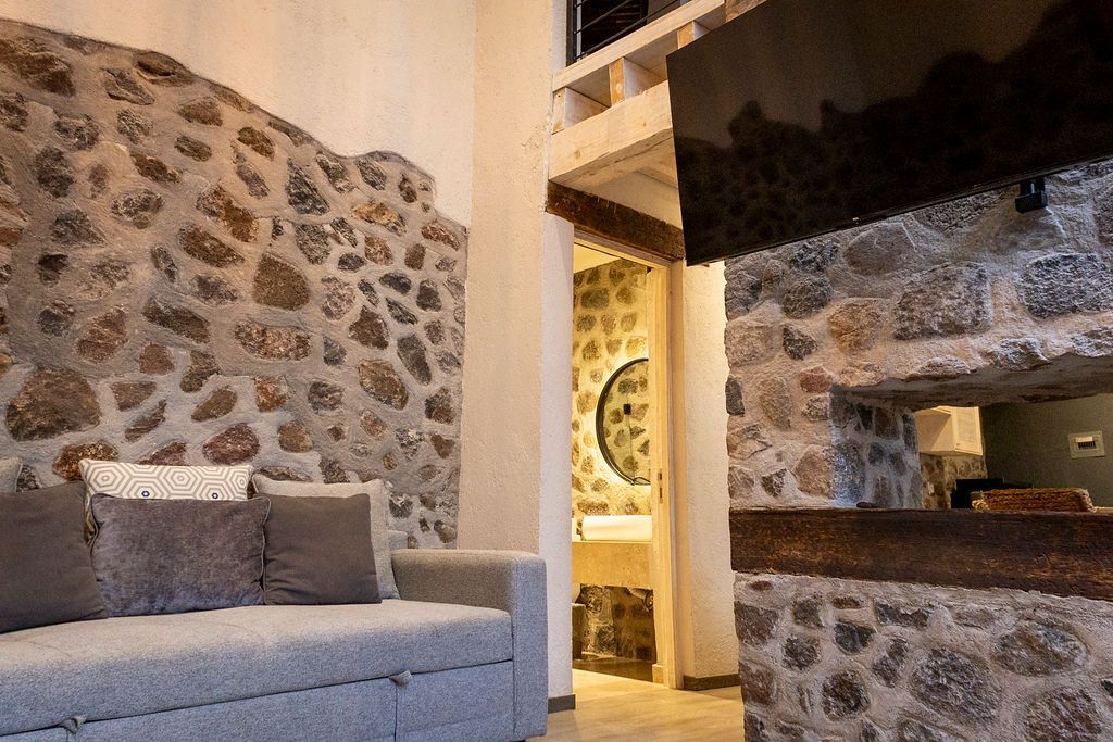 Gray sofa against a stone wall in a room with a glimpse of a bathroom.