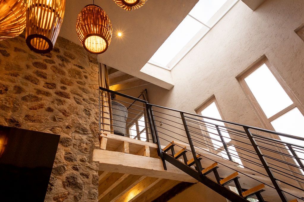 Interior with stone wall, stairs with metal railing, skylight, and woven light fixtures.