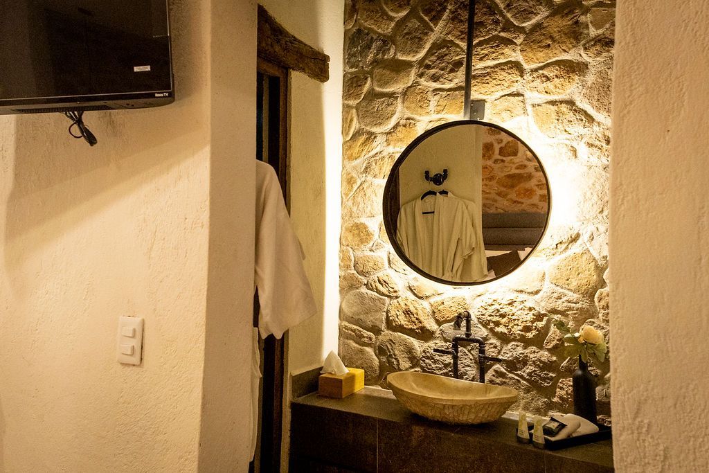 Bathroom with stone wall, round mirror, and vessel sink.