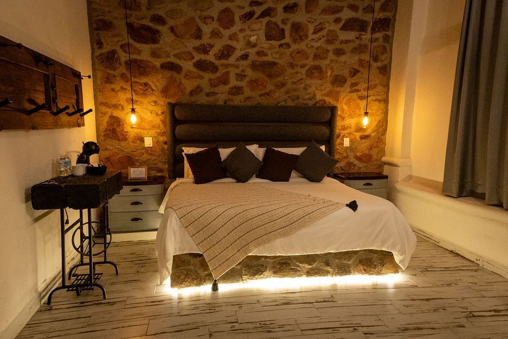 Cozy bedroom with stone wall, bed with light-up base, bedside tables, and warm lighting.