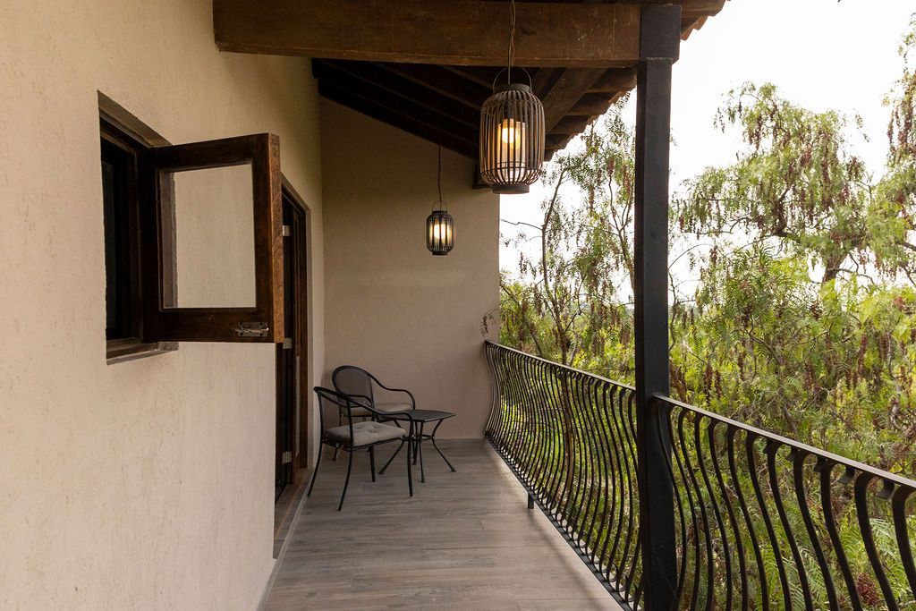 Balcony with wrought iron railing, chairs, and lanterns. A window is open with trees in the background.