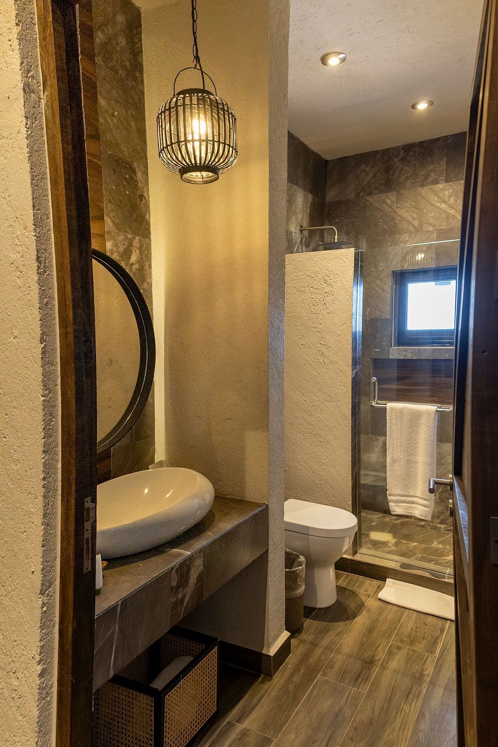 Bathroom with sink, toilet, and shower. Rustic design with pendant light, round mirror, and wood accents.
